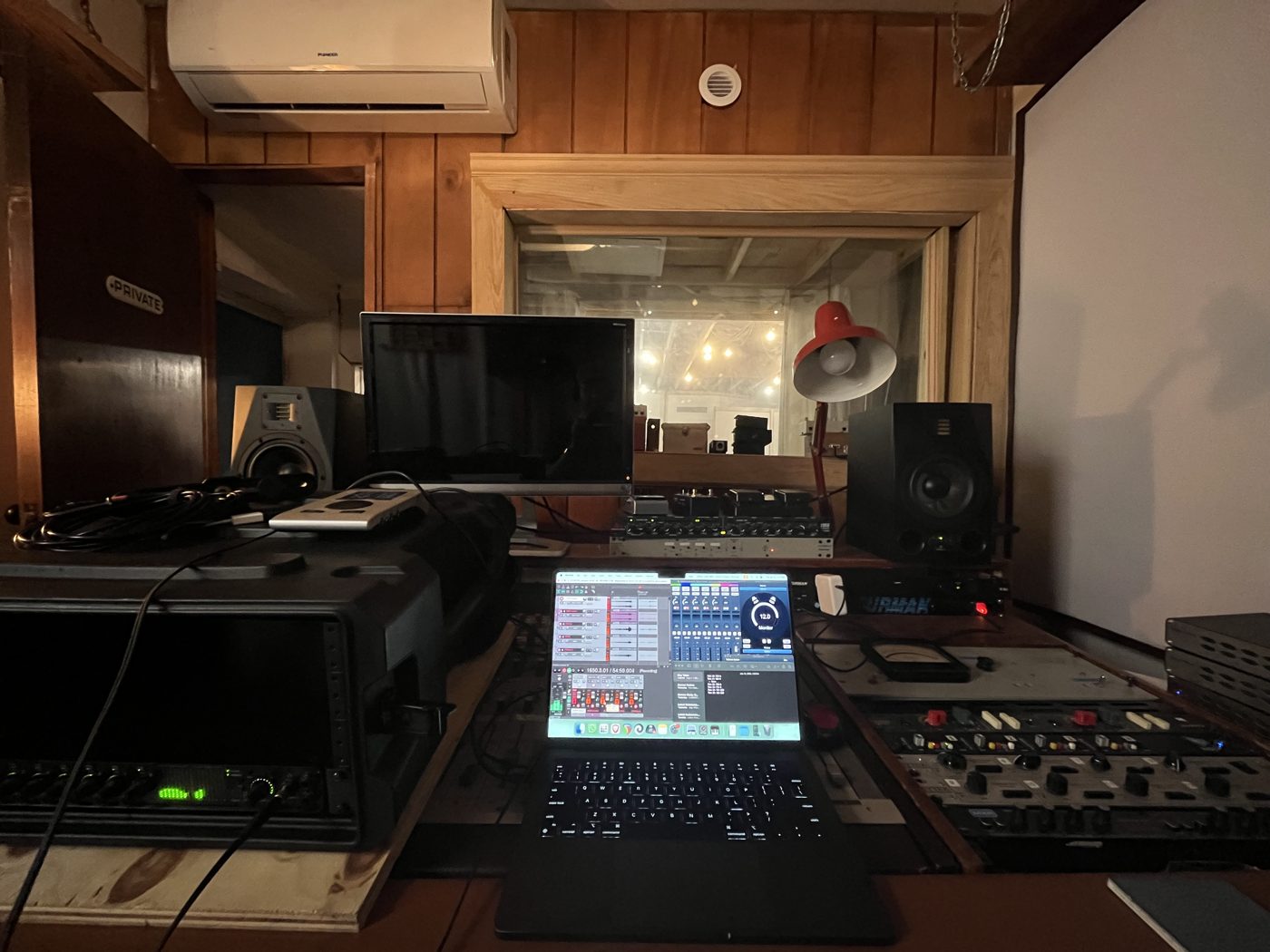 Studio control room with monitors, outboard gear, and a laptop running a DAW session