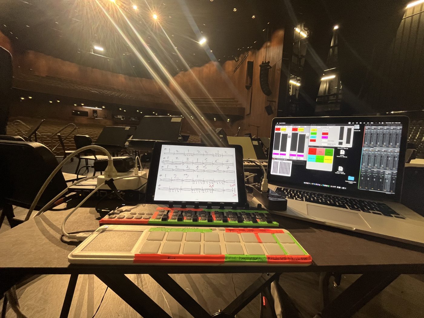 Laptop, iPad score, and MIDI controllers on a table in a concert hall